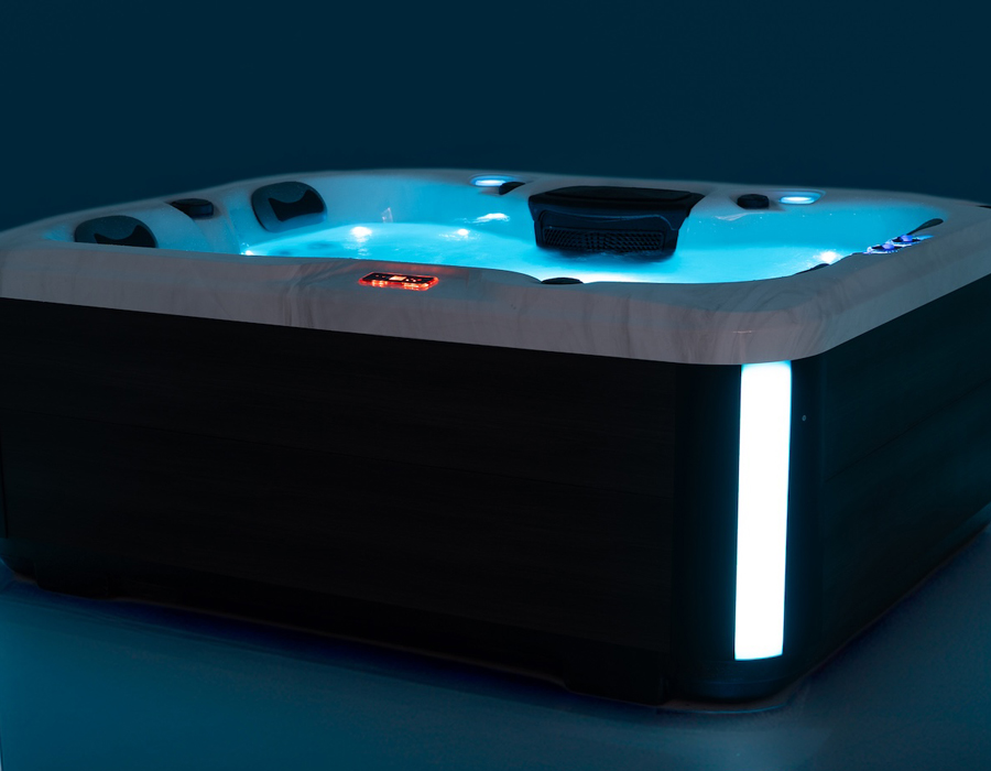 A close-up view of a lit CORE budget hot tub with glowing blue water, headrests, illuminated controls, and accent lights.