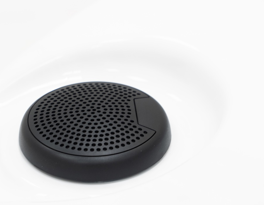 Close-up of a built-in round, black bluetooth hot tub speaker with perforated holes, set against a smooth white surface.