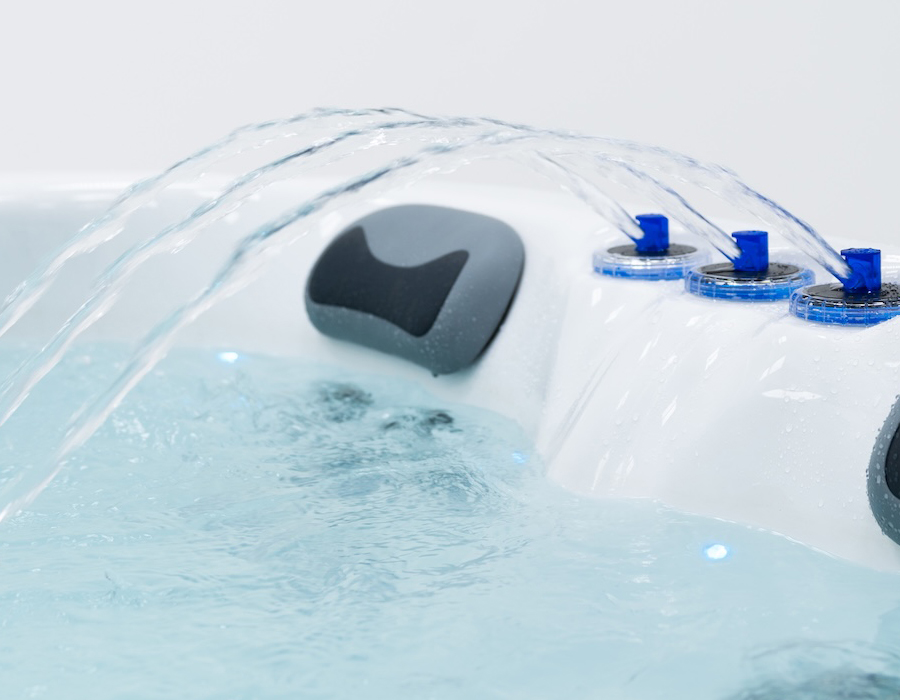 Water streams gracefully into a clear hot tub, surrounded by sleek design and blue controls, conveying a sense of relaxation and modern luxury.