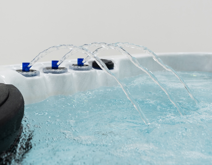 Water streams gracefully into a clear hot tub, surrounded by sleek design and blue controls, conveying a sense of relaxation and modern luxury.