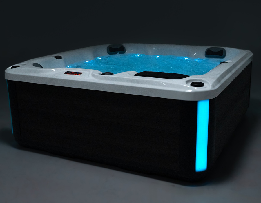 A close-up view of a lit Pulse 6 seater budget hot tub with glowing blue water, headrests, illuminated controls, and accent lights.