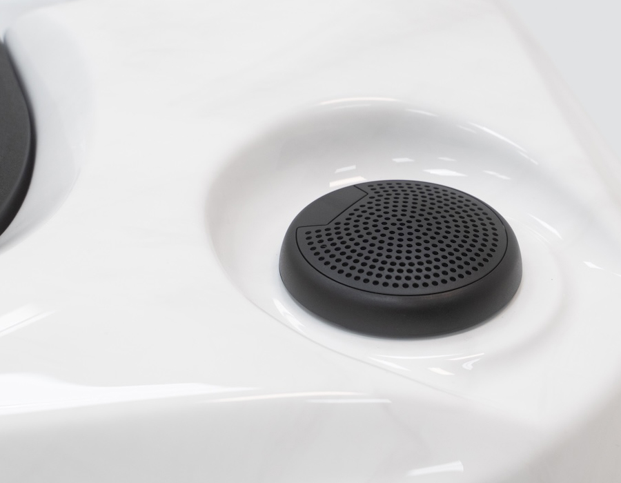 Close-up of a built-in round, black bluetooth hot tub speaker with perforated holes, set against a smooth white surface.