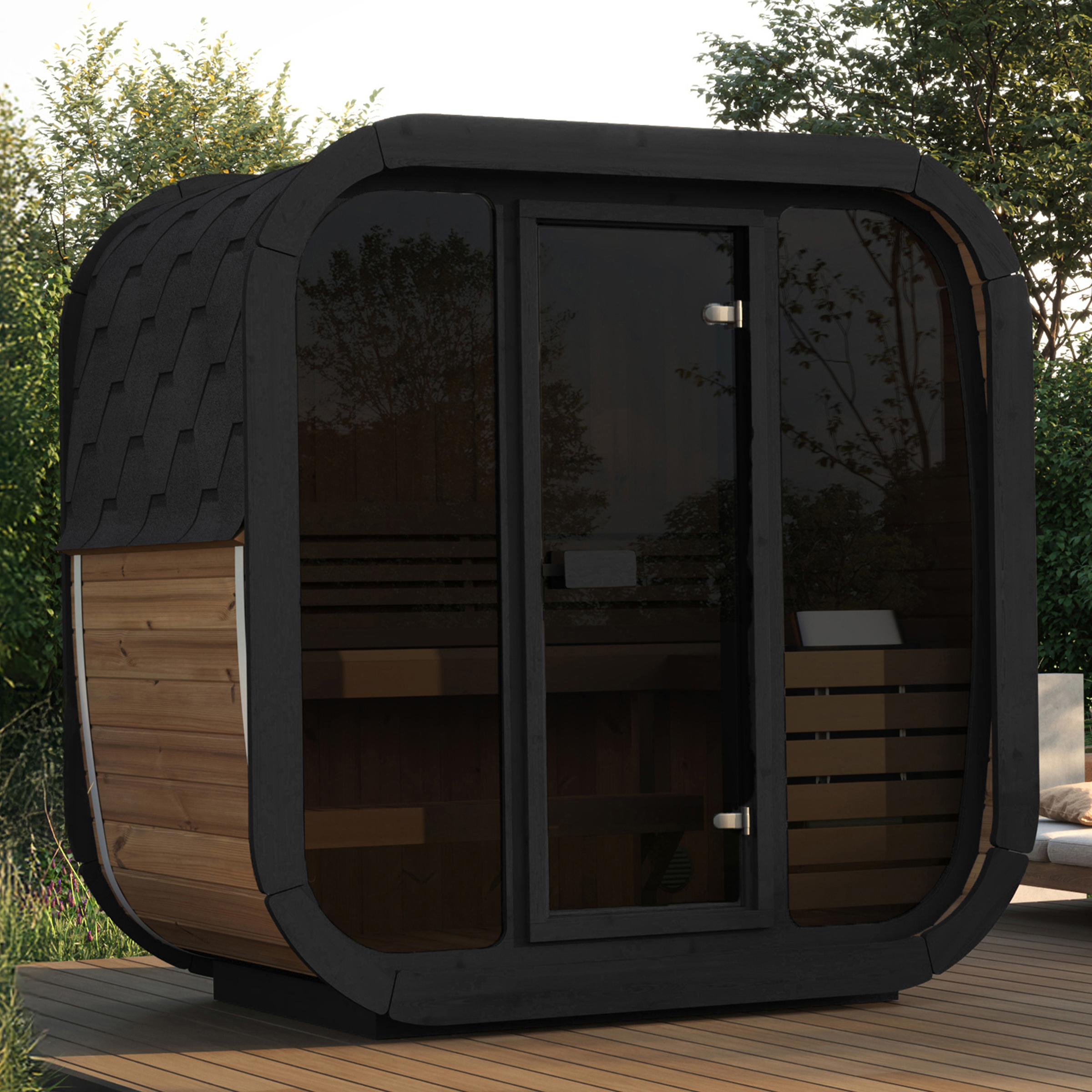 A small modern wooden sauna with tinted glass door on a wooden deck is surrounded by lush greenery. Nearby are cushioned chairs, creating a serene outdoor setting.